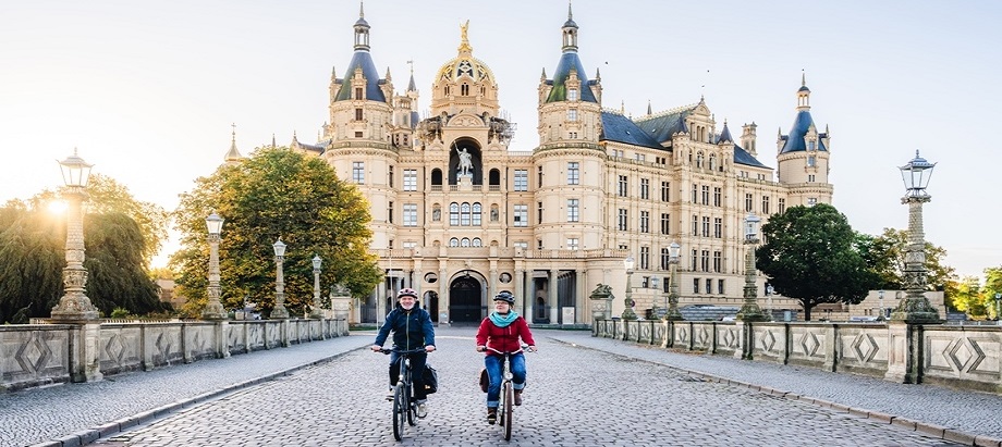 Das Schweriner Schloss zum Sonnenaufgang im Herbst mit Radfahrern TMV Gross header
